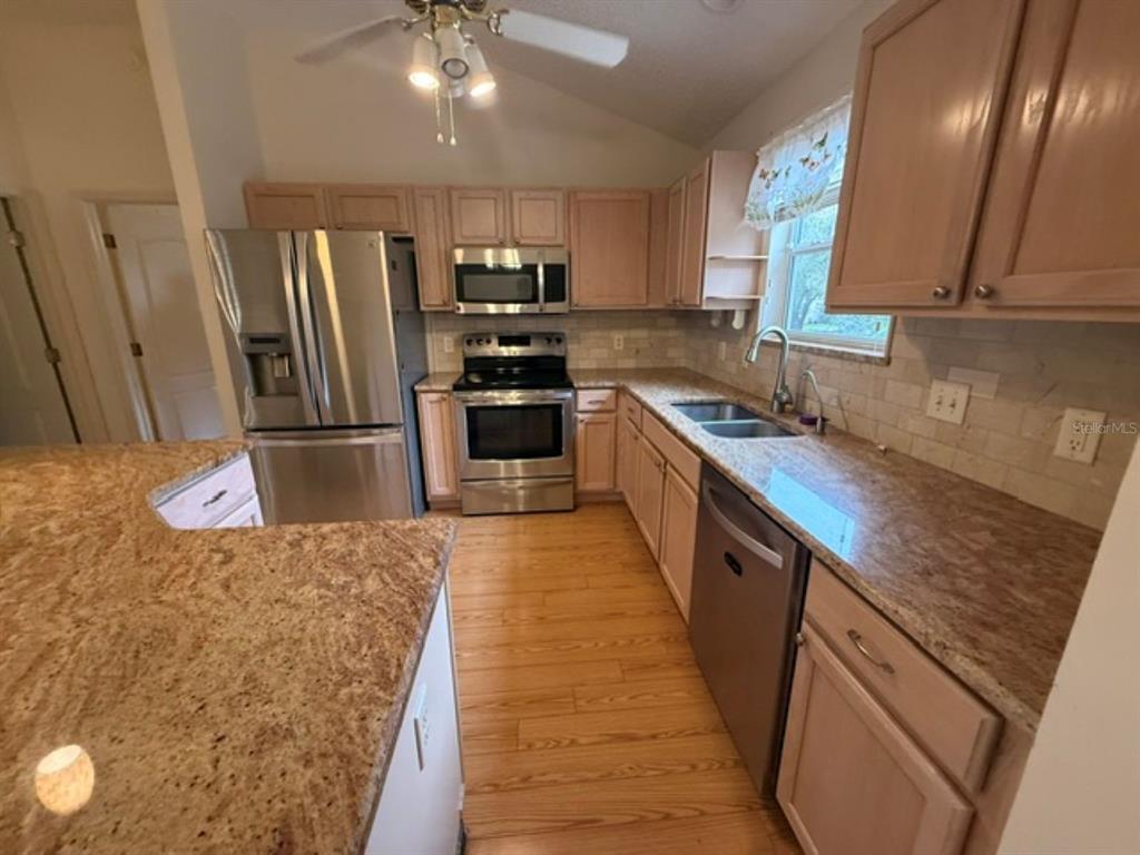 A kitchen with light wood cabinets, granite countertops, stainless steel appliances, and wood-look flooring — 3105 BERWYN WAY, THE VILLAGES, FL