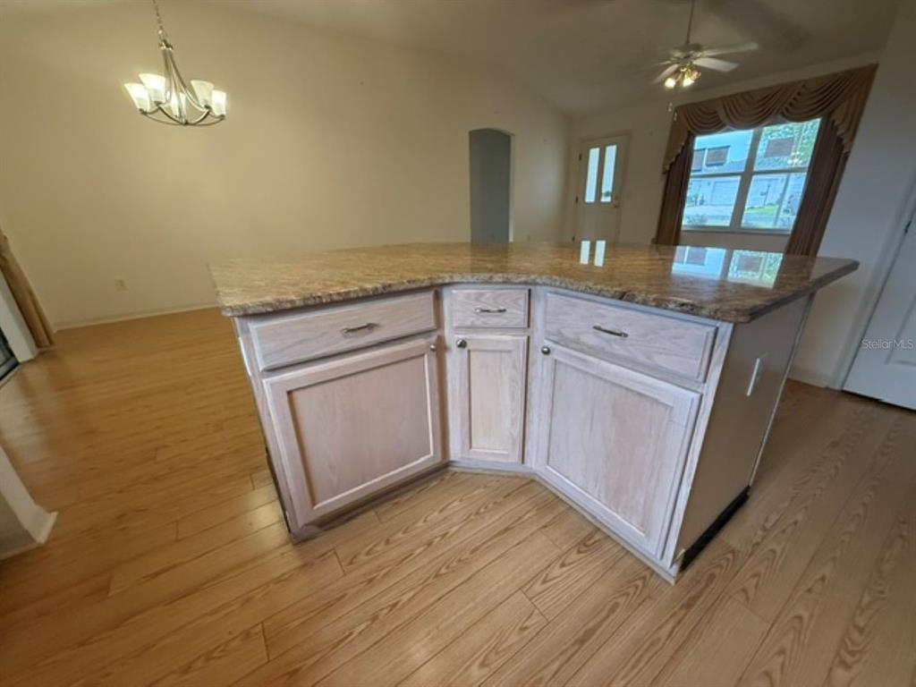 A kitchen island with light wood cabinets and a granite countertop sits on hardwood floors — 3105 BERWYN WAY, THE VILLAGES, FL
