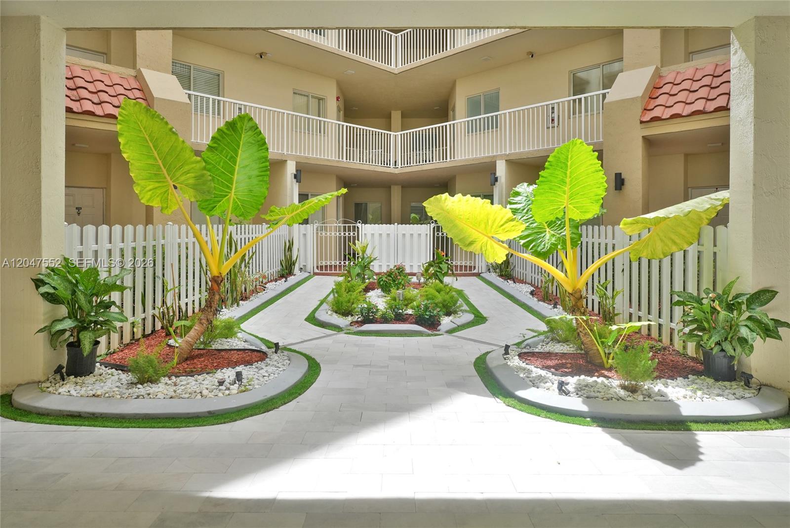 A paved courtyard features two large potted plants, white picket fencing, and a multi-story building — 10720 NW 66th St # 205, Doral FL 33178, DORAL, FL