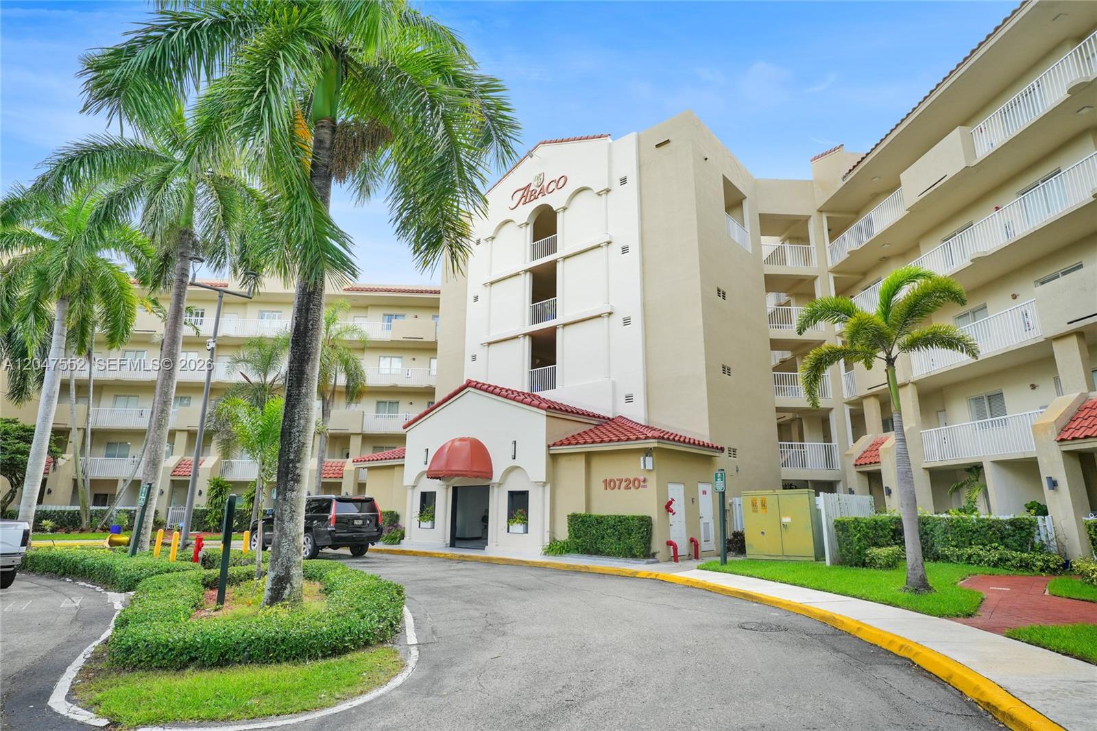 An exterior view of a multi-story apartment building with palm trees and a paved driveway — 10720 NW 66th St # 205, Doral FL 33178, DORAL, FL