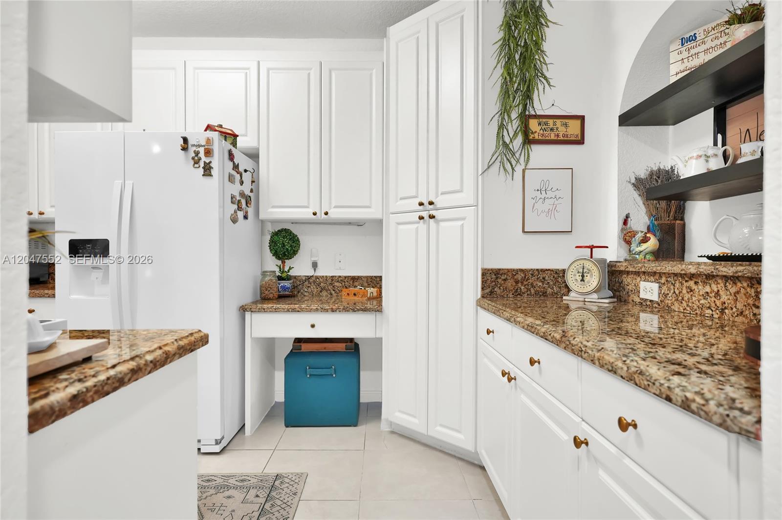 A kitchen features white cabinetry, granite countertops, a built-in desk area, and a white refrigerator — 10720 NW 66th St # 205, Doral FL 33178, DORAL, FL
