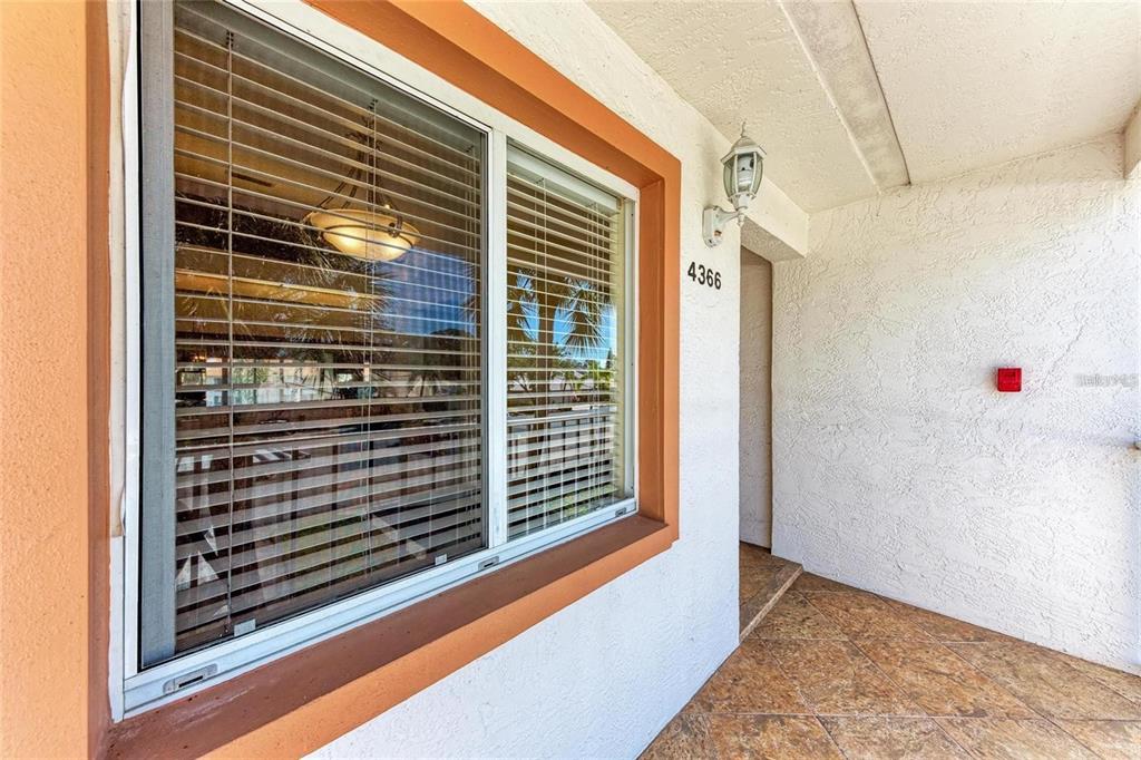 A view of a building exterior featuring a window with blinds and a tiled porch — 4366 MADEIRA COURT UNIT 3356, SARASOTA, FL