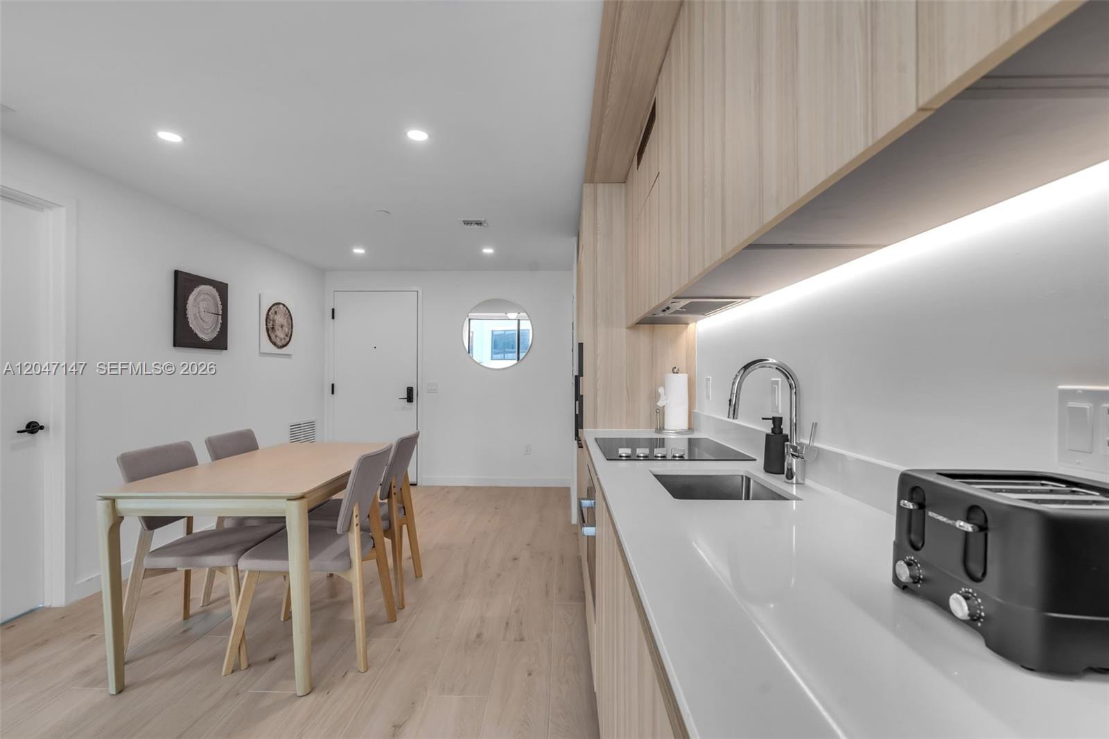 A modern kitchen features light wood cabinetry, white countertops, and an adjacent dining area — 225 N Miami Ave # 1107, Miami FL 33128, MIAMI, FL