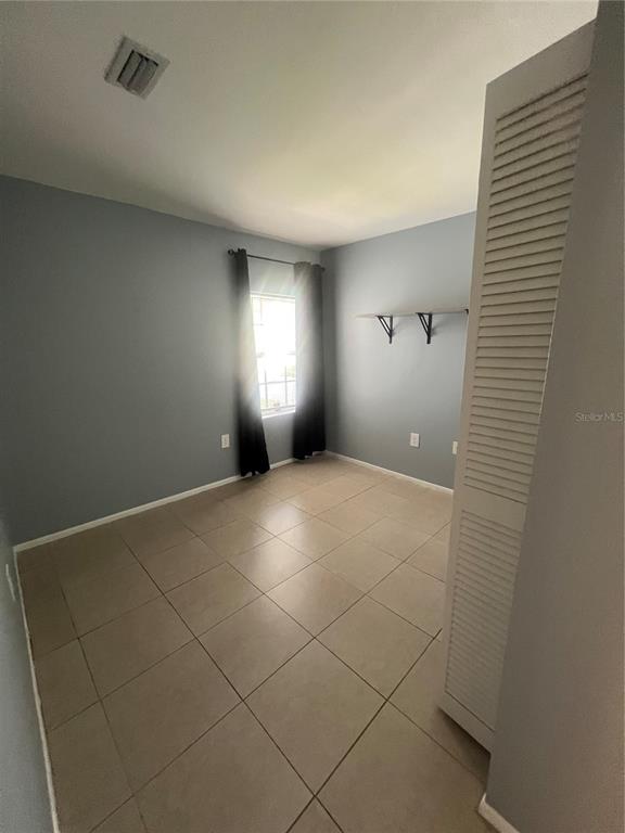 A bedroom with gray walls, tile flooring, a window with dark curtains, and wall-mounted shelves — 215 GOLDSTEIN STREET UNIT 4, PUNTA GORDA, FL