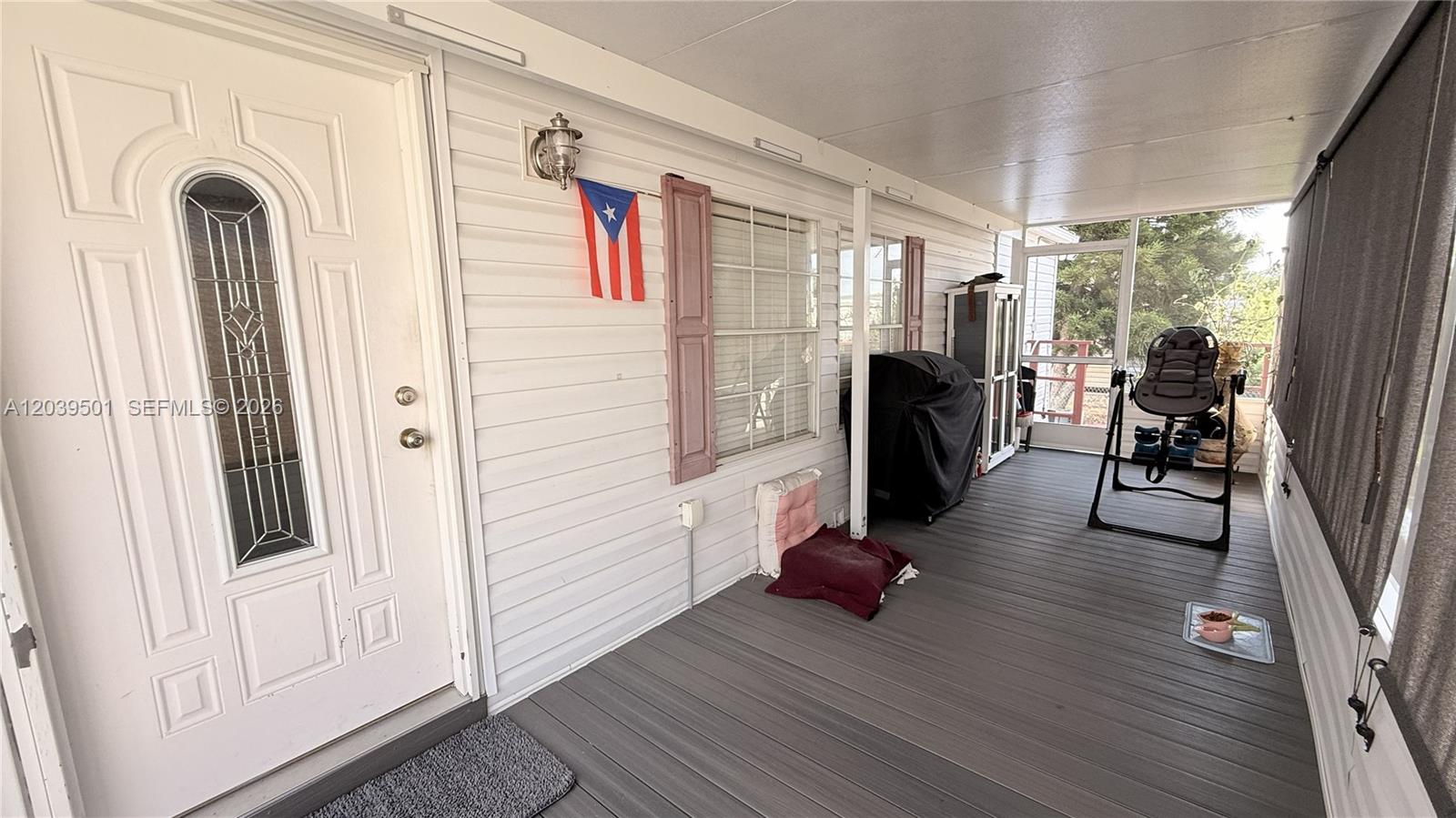 A covered porch features white siding, a front door, a Puerto Rican flag, and furniture — 8631 SW 18th Pl, Davie FL 33324, DAVIE, FL