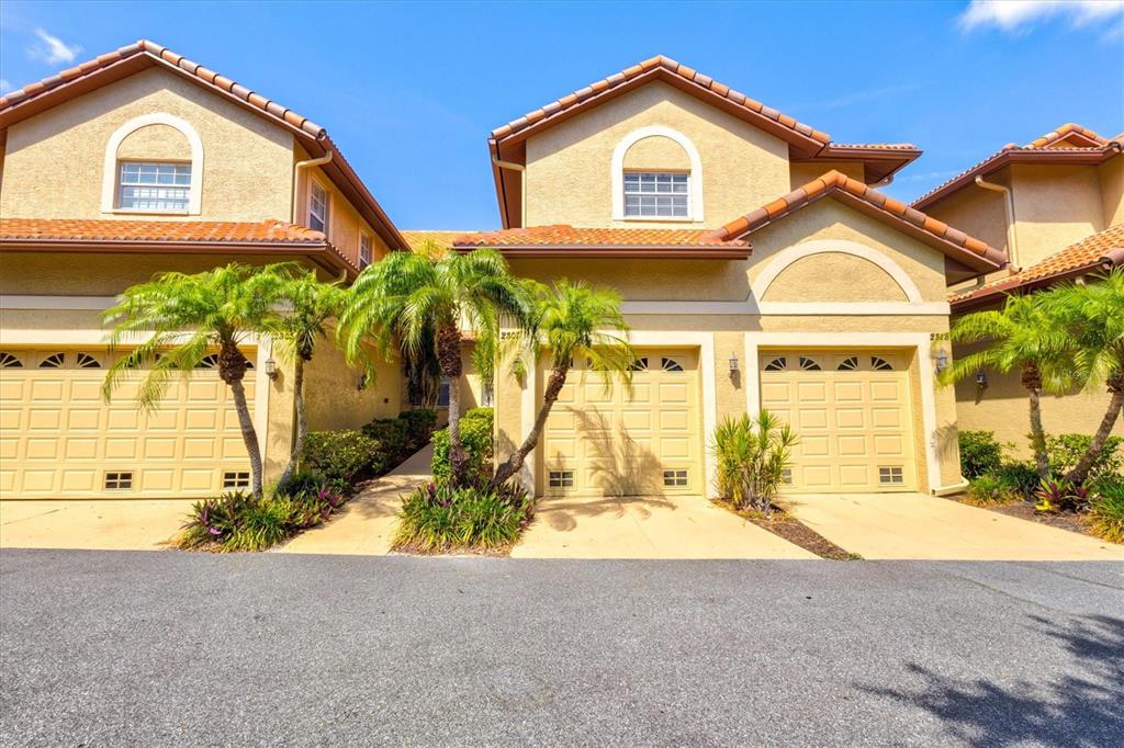A row of three tan townhomes with arched windows and attached garages under a blue sky — 2309 JESSIE HARBOR DRIVE UNIT 2402, OSPREY, FL