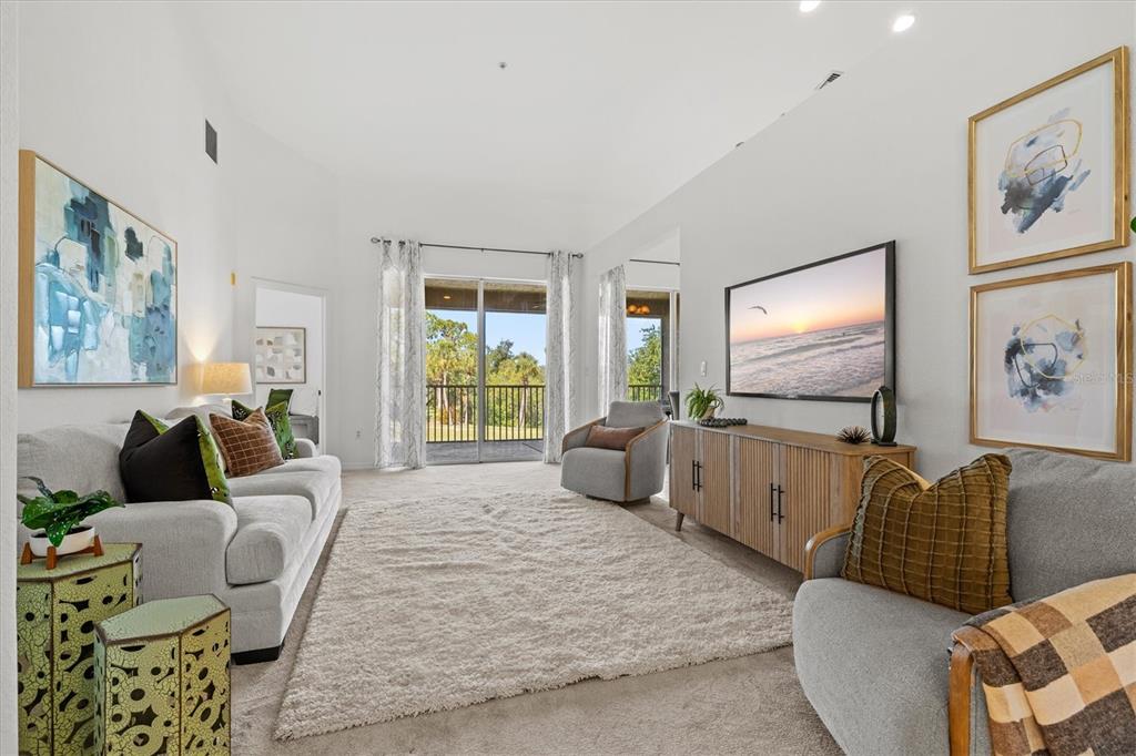 A living room features a sofa, armchairs, a television, and a balcony with outdoor views — 2309 JESSIE HARBOR DRIVE UNIT 2402, OSPREY, FL