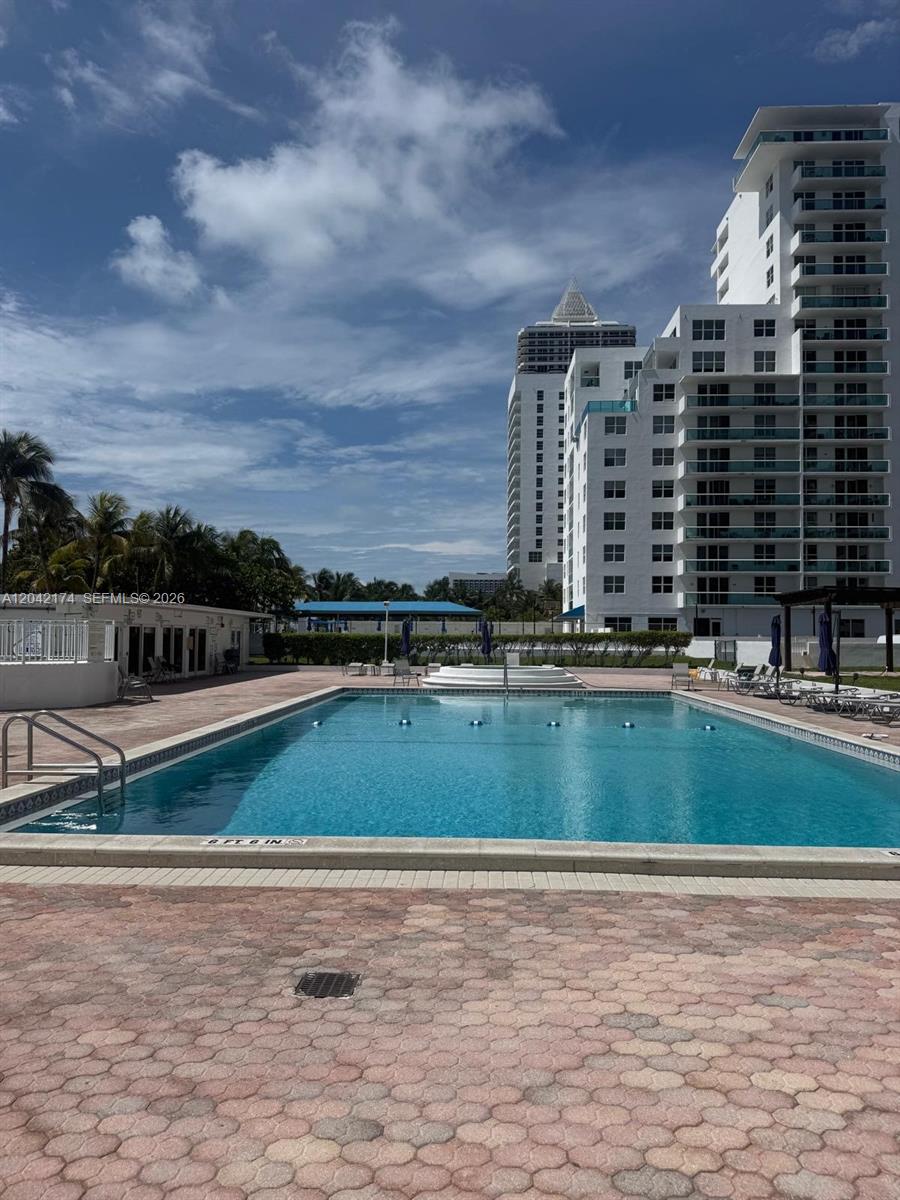 A rectangular swimming pool sits on a paved deck in front of a tall apartment building — 5005 Collins Ave # 1104, Miami Beach FL 33140, MIAMI BEACH, FL