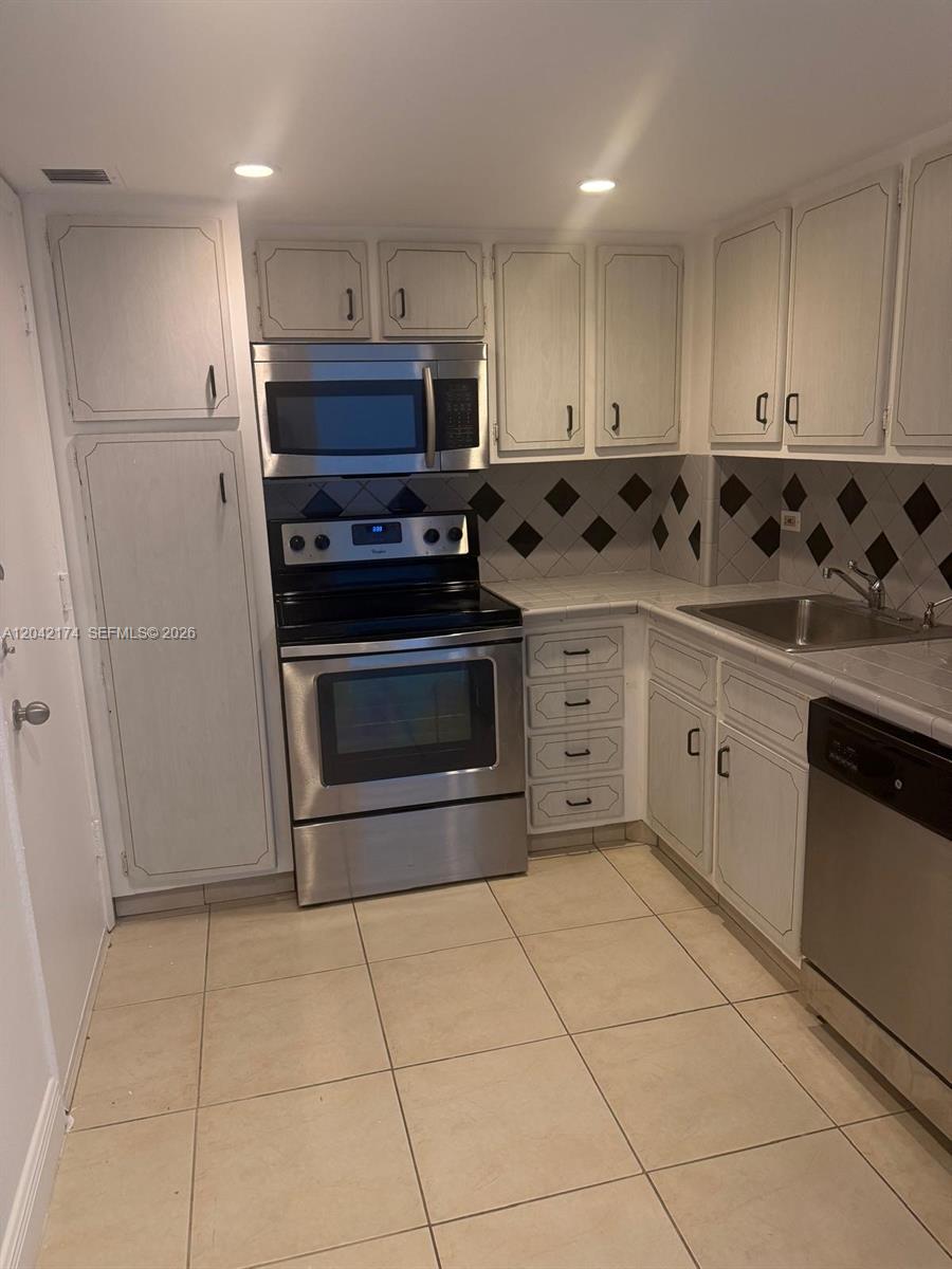 A kitchen features white cabinets, stainless steel appliances, a tiled backsplash, and light floor tiles — 5005 Collins Ave # 1104, Miami Beach FL 33140, MIAMI BEACH, FL