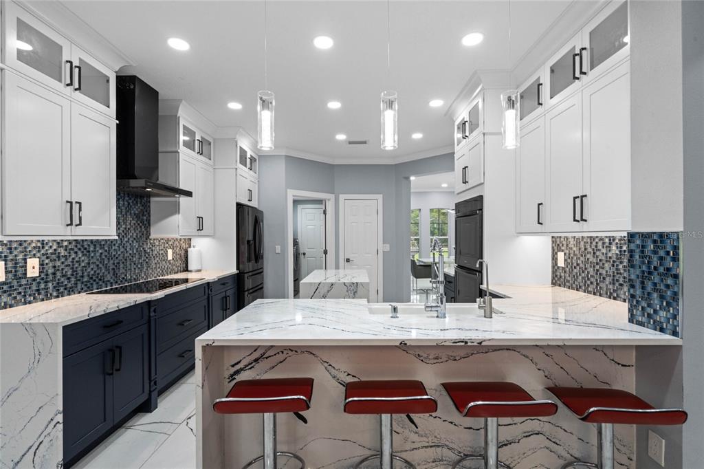 A modern kitchen features white upper cabinets, dark lower cabinets, marble countertops, and red bar stools — 6607 WHISPERING PINES ROAD, ORLANDO, FL