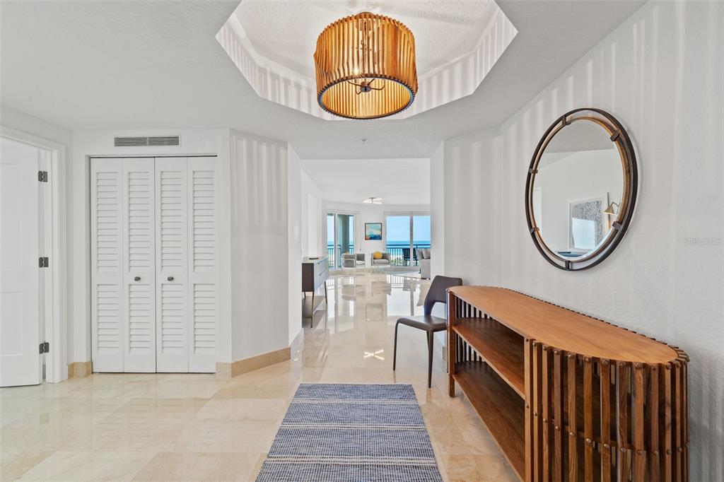 A bright foyer features a wooden slatted light fixture, a console table, and tile flooring — 1180 GULF BOULEVARD UNIT 401, CLEARWATER BEACH, FL