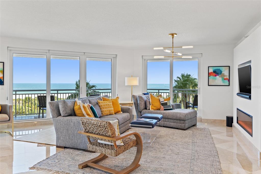 A living room features gray sofas, a woven chair, and large windows overlooking the ocean — 1180 GULF BOULEVARD UNIT 401, CLEARWATER BEACH, FL