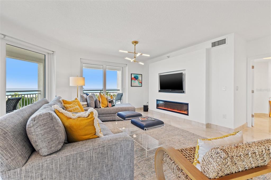 A living room features a grey sectional sofa, a fireplace, a television, and balcony views — 1180 GULF BOULEVARD UNIT 401, CLEARWATER BEACH, FL