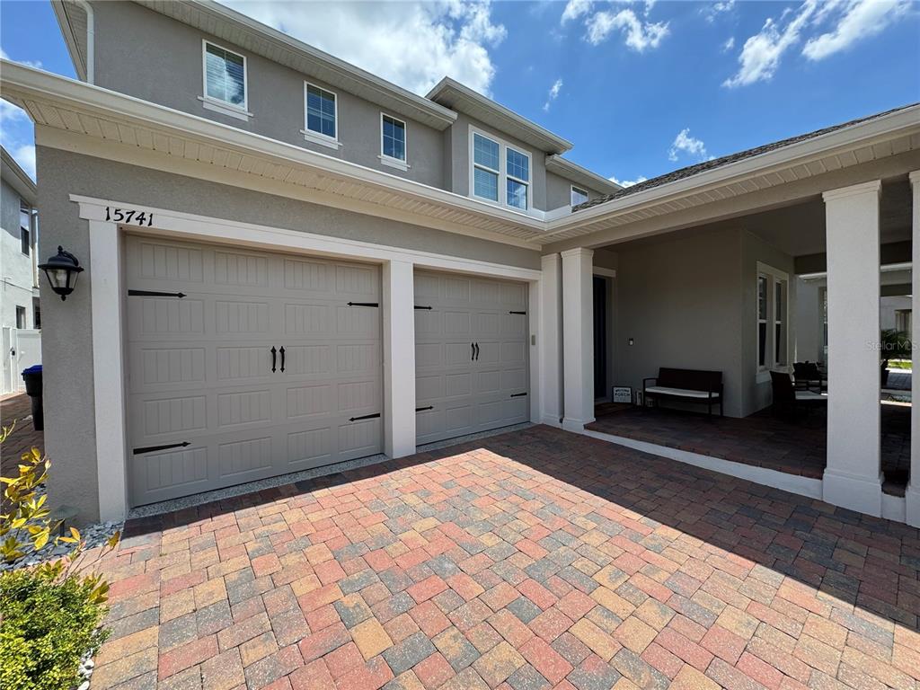 A two-car garage with a paver driveway and a covered front porch entrance — 15741 SWEET LEMON WAY, WINTER GARDEN, FL