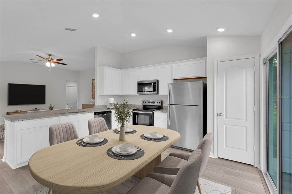 A bright kitchen features white cabinets, stainless steel appliances, and a light wood dining table — 560 MARION OAKS MANOR, OCALA, FL