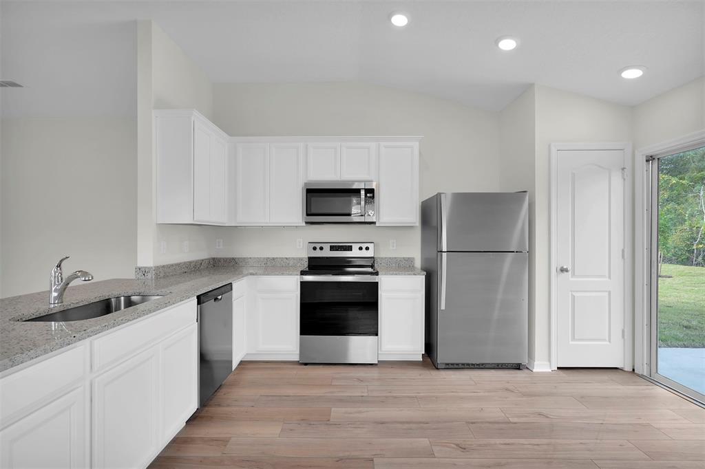 A kitchen with white cabinets, granite countertops, stainless steel appliances, and light wood-look flooring — 560 MARION OAKS MANOR, OCALA, FL