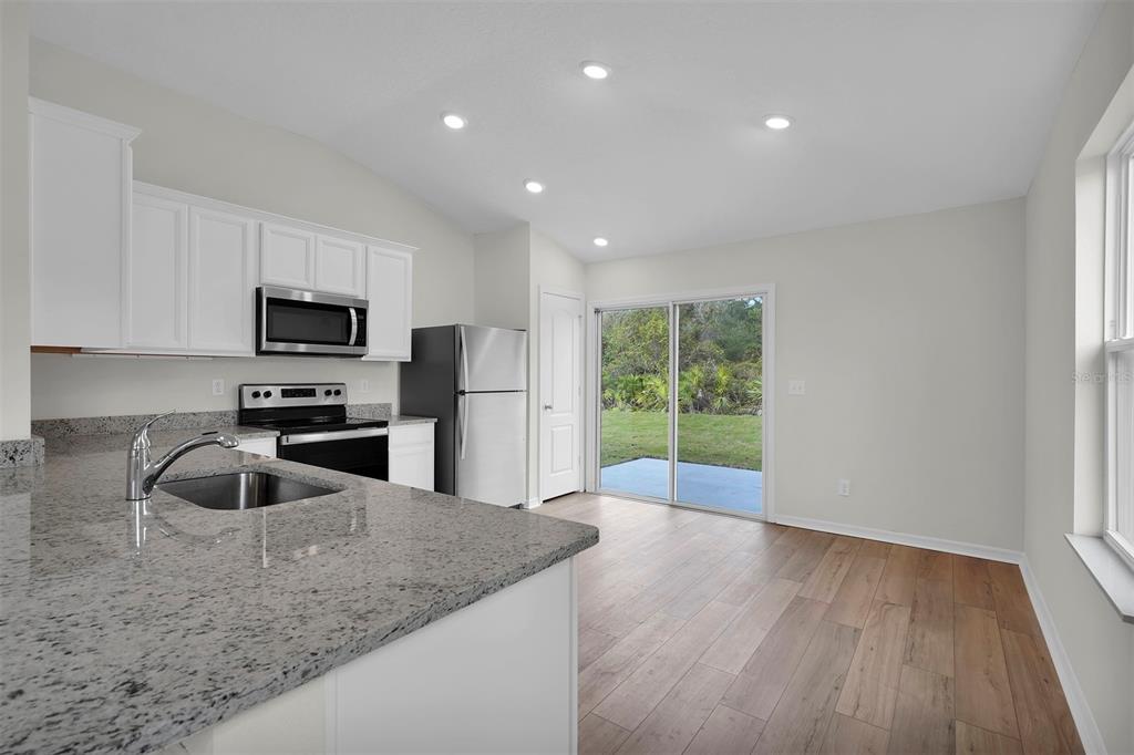 A kitchen with granite countertops and white cabinets opens to a dining area with sliding doors — 560 MARION OAKS MANOR, OCALA, FL