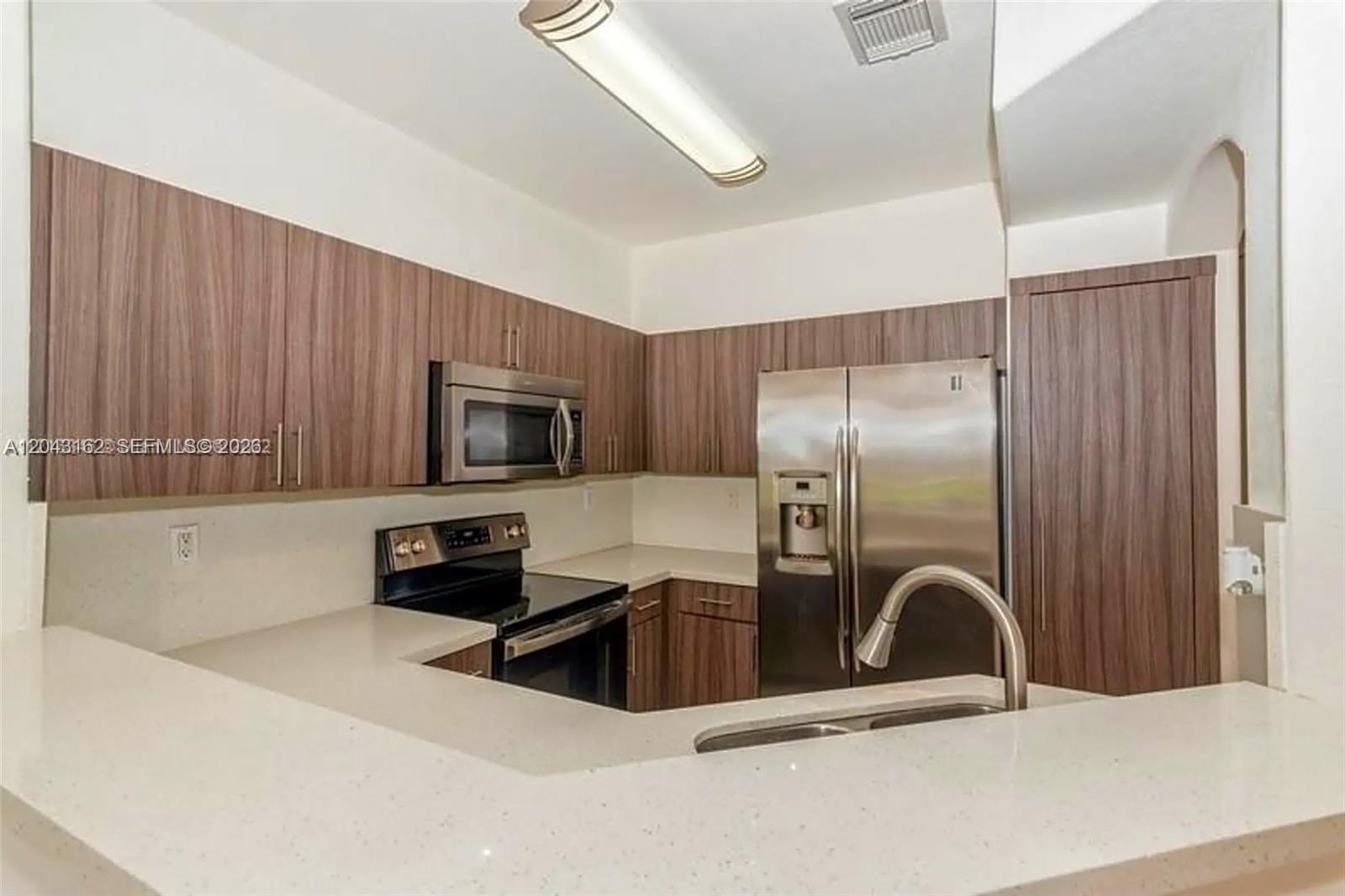 A kitchen features wood-grain cabinets, stainless steel appliances, and white countertops — 11497 NW 78th Ter, Doral FL 33178, DORAL, FL