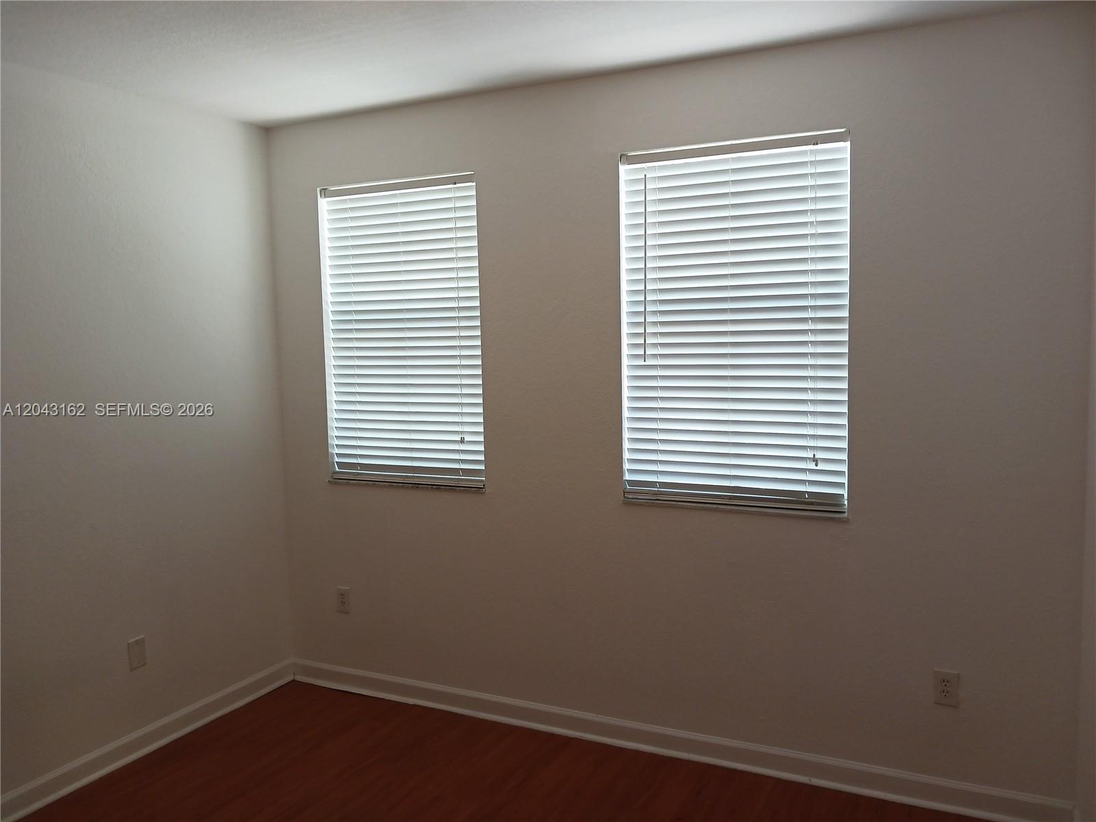 An empty room features white walls, wood-look flooring, and two windows with white blinds — 11497 NW 78th Ter, Doral FL 33178, DORAL, FL