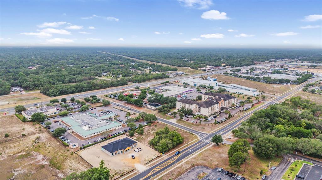 An aerial view shows commercial buildings, a hotel, and parking lots surrounded by wooded areas — 00 QUALITY DRIVE, SPRING HILL, FL
