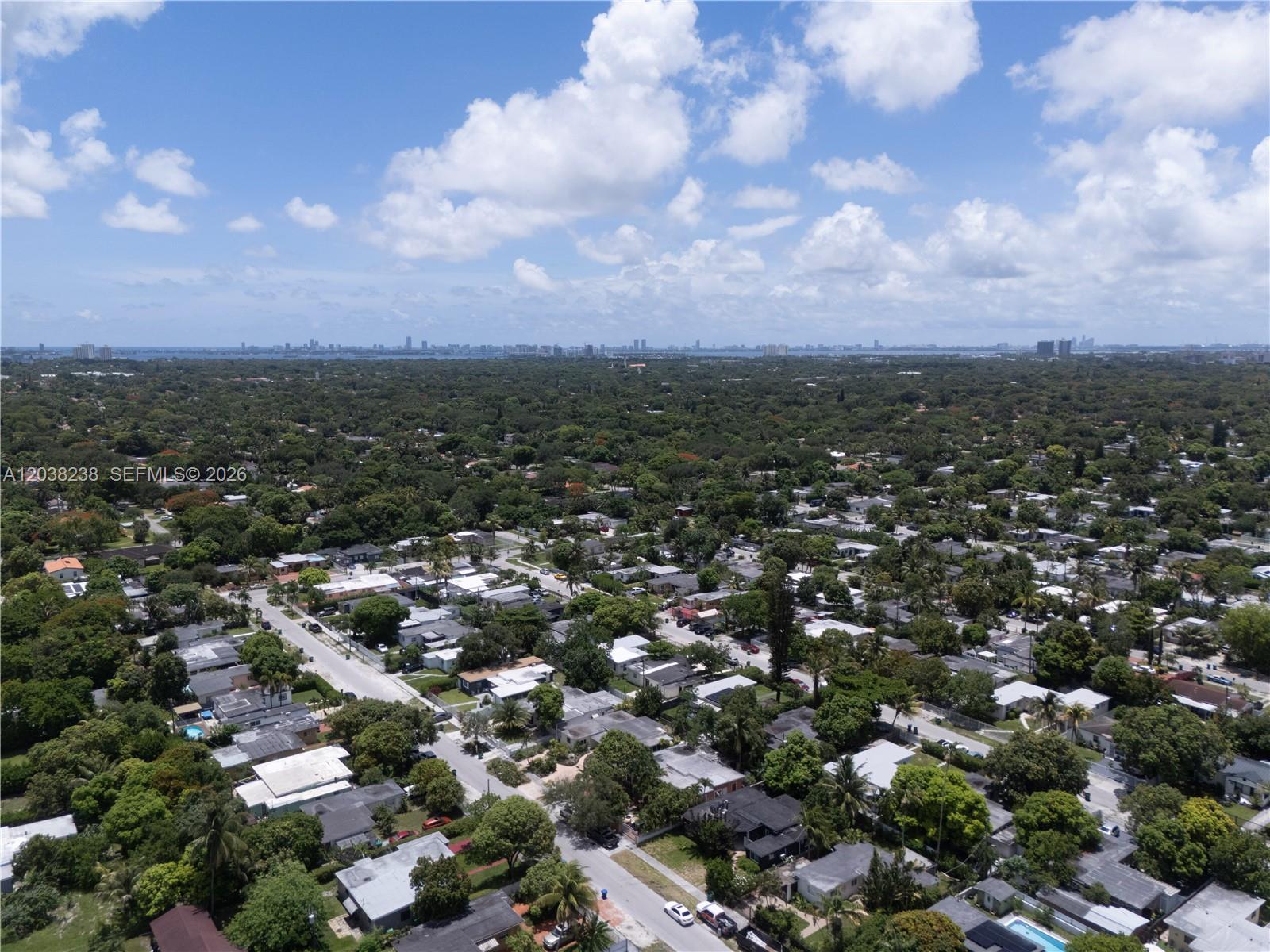 An aerial view shows a residential neighborhood with many trees and a distant city skyline — 334 NW 110th St, Miami FL 33168, MIAMI, FL