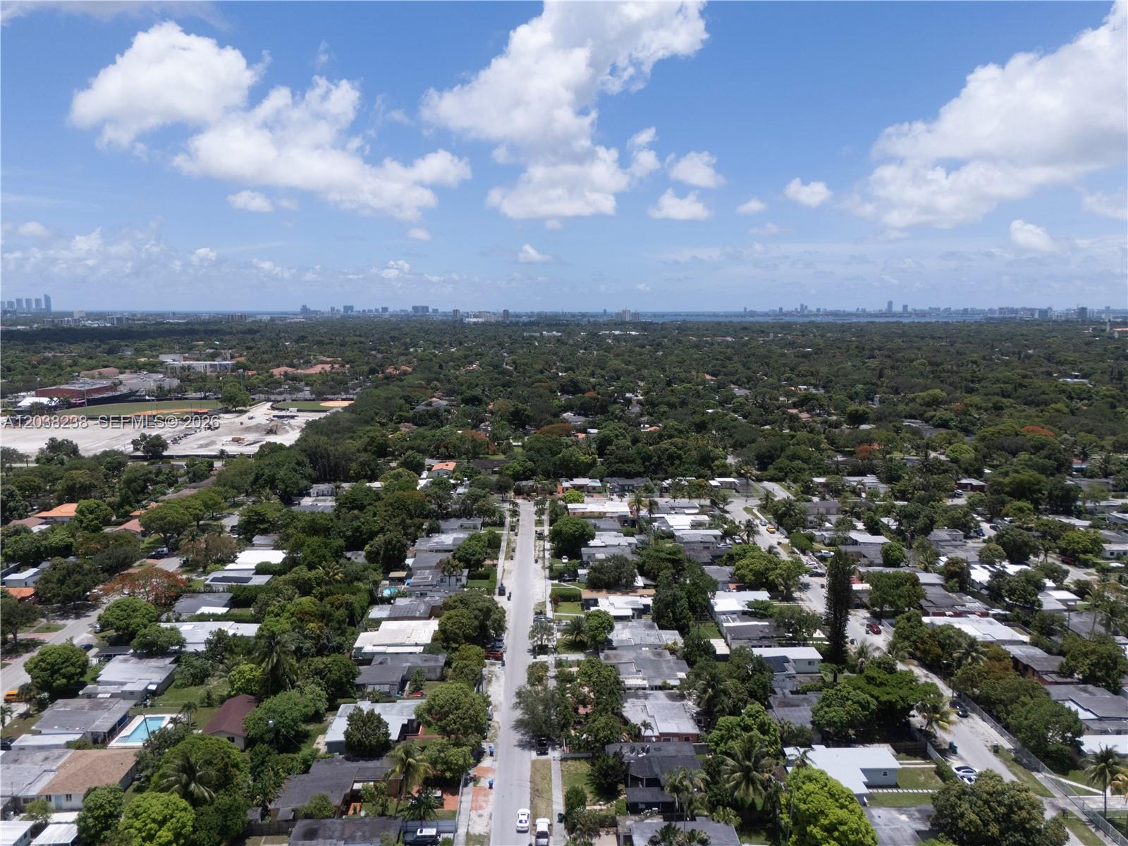 An aerial view shows a residential neighborhood with many trees and a distant city skyline — 334 NW 110th St, Miami FL 33168, MIAMI, FL