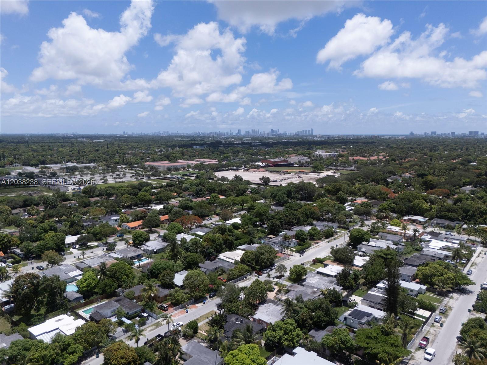 An aerial view shows a suburban neighborhood with many trees and a distant city skyline — 334 NW 110th St, Miami FL 33168, MIAMI, FL