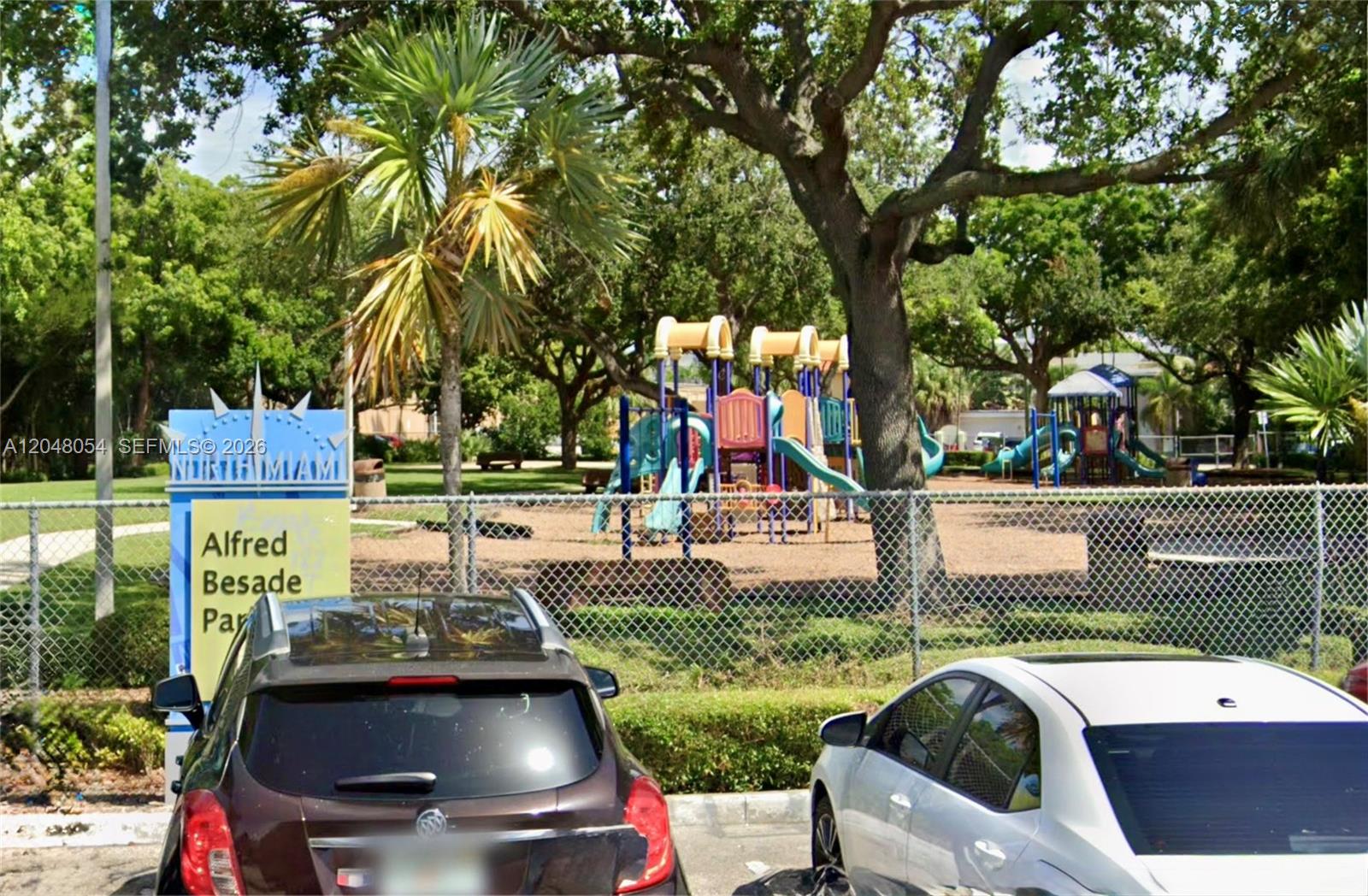 A playground with colorful equipment is visible behind a chain-link fence at a public park — 1855 NE 121st St # 16, North Miami FL 33181, NORTH MIAMI, FL