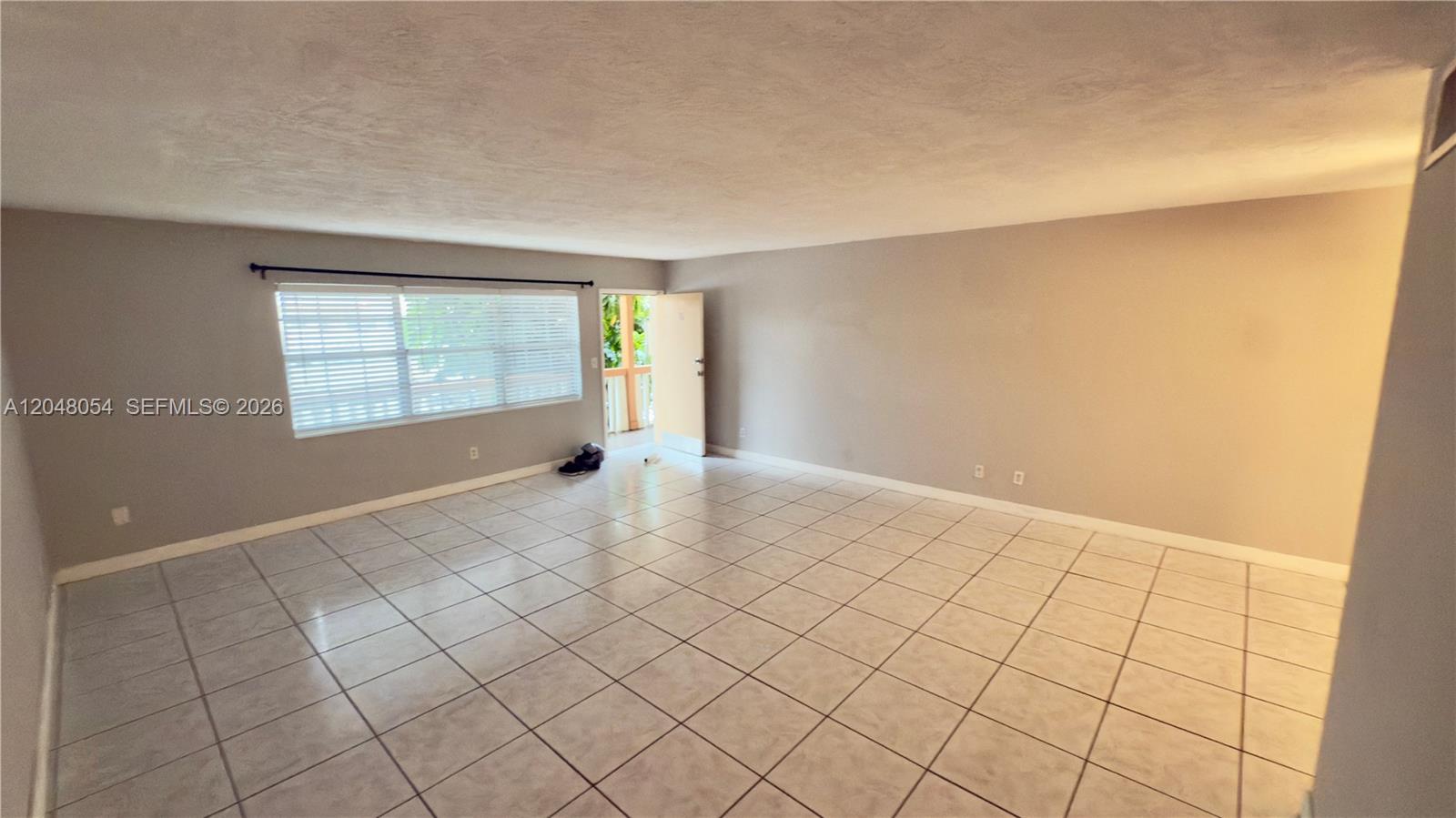An empty room features light-colored tile flooring, gray walls, and a window with blinds — 1855 NE 121st St # 16, North Miami FL 33181, NORTH MIAMI, FL
