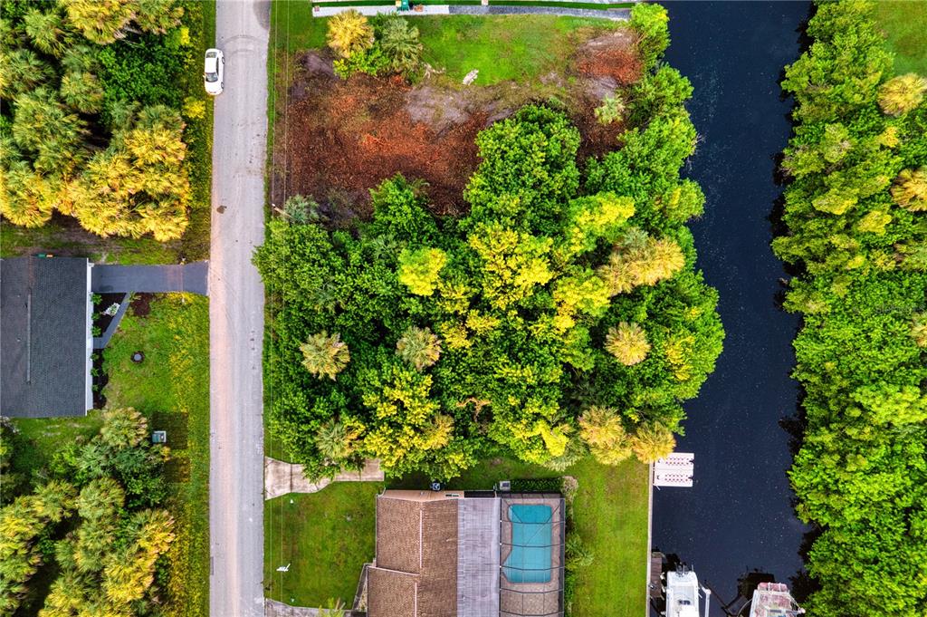 An aerial view shows a vacant lot with dense trees situated between a road and a canal — 18522 AYRSHIRE CIRCLE, PORT CHARLOTTE, FL