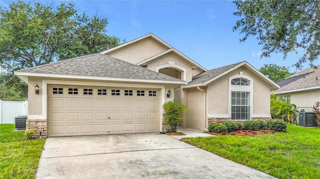 A single-story house with a two-car garage, tan stucco siding, and a stone-accented exterior — 7016 JAMESTOWN MANOR DRIVE, RIVERVIEW, FL