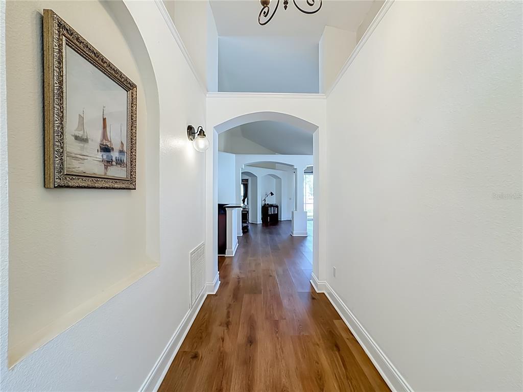 A hallway with wood-look flooring leads through arched doorways toward a bright living area — 7016 JAMESTOWN MANOR DRIVE, RIVERVIEW, FL