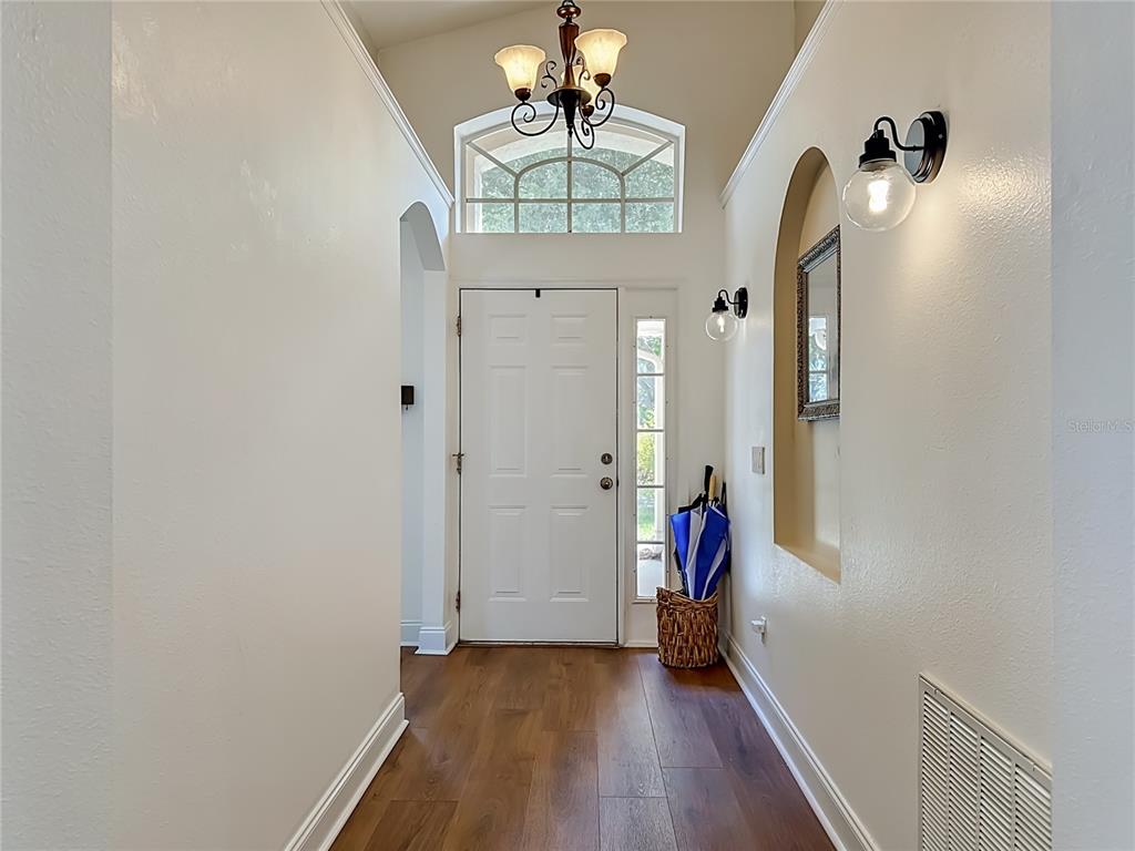 A bright entryway features wood-look flooring, a white front door, and a decorative wall niche — 7016 JAMESTOWN MANOR DRIVE, RIVERVIEW, FL