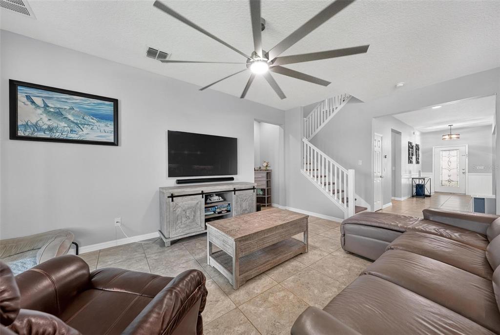 A living room features a large sectional sofa, a coffee table, a television, and stairs — 1464 CABOT DRIVE, CLERMONT, FL