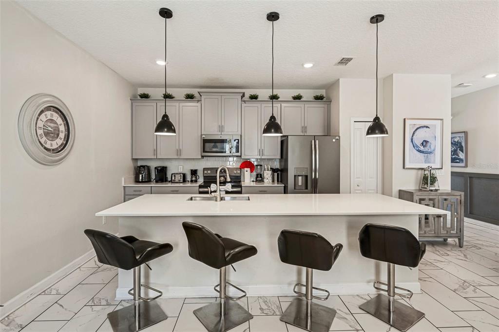 A kitchen features a white island with four bar stools, gray cabinets, and pendant lighting — 218 OCEAN COURSE AVENUE, DAVENPORT, FL