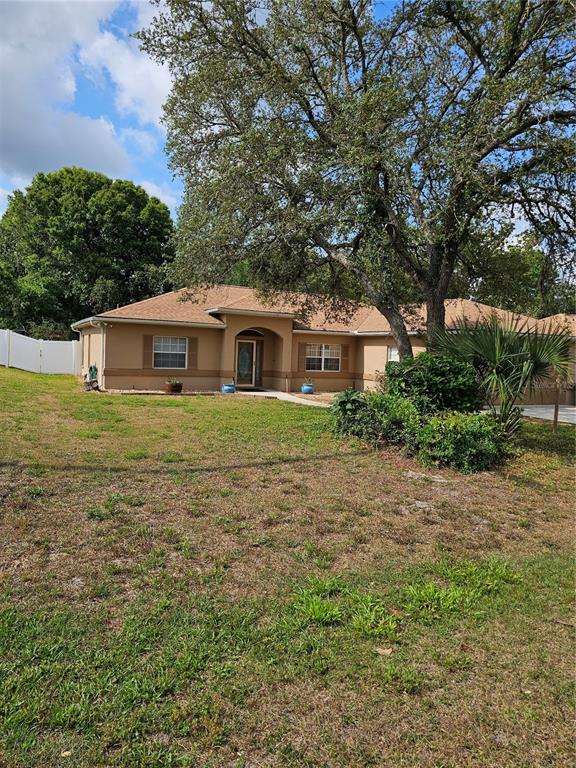A single-story tan house with a brown roof sits behind a large tree and lawn — 5280 SW 88TH PLACE, OCALA, FL