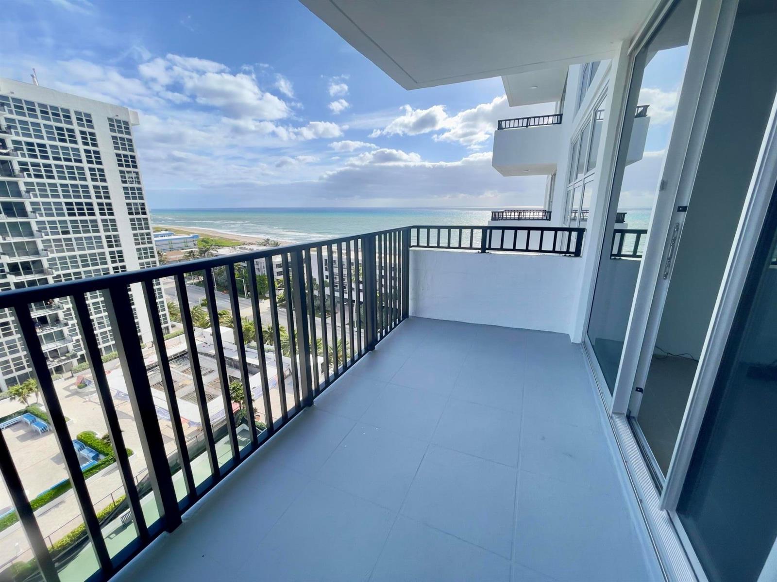 A balcony with gray tile flooring and black railings overlooks the ocean and city buildings — 525 N Ocean Boulevard # 1422, Pompano Beach FL 33062, POMPANO BEACH, FL