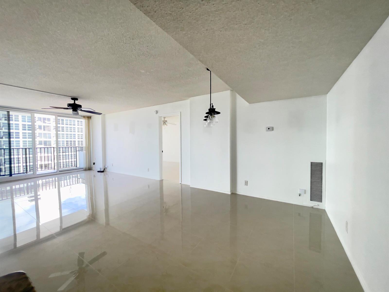 An empty living area features white walls, beige tile flooring, a ceiling fan, and balcony access — 525 N Ocean Boulevard # 1422, Pompano Beach FL 33062, POMPANO BEACH, FL