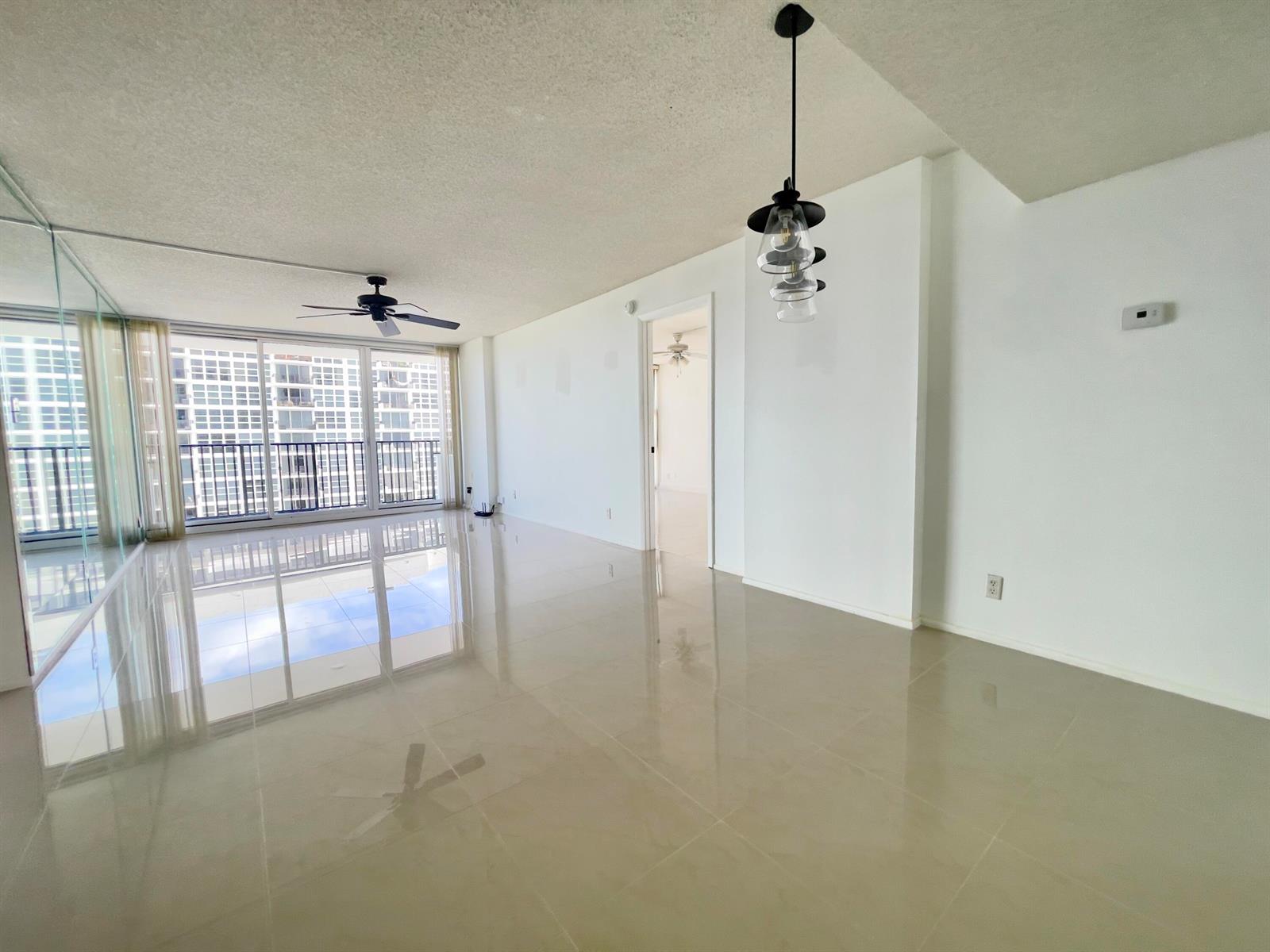 An empty living area with beige tile floors, a ceiling fan, and a glass balcony door — 525 N Ocean Boulevard # 1422, Pompano Beach FL 33062, POMPANO BEACH, FL