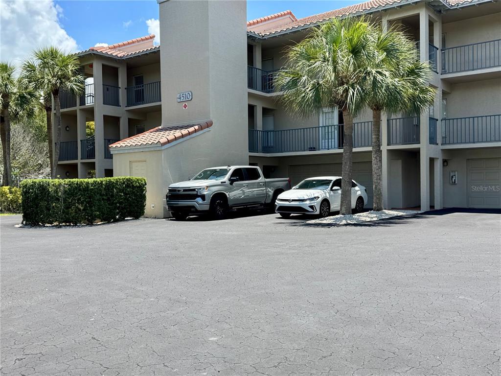 A multi-story apartment building exterior features a parking area with two cars and palm trees — 4510 EL CONQUISTADOR PARKWAY UNIT 204, BRADENTON, FL