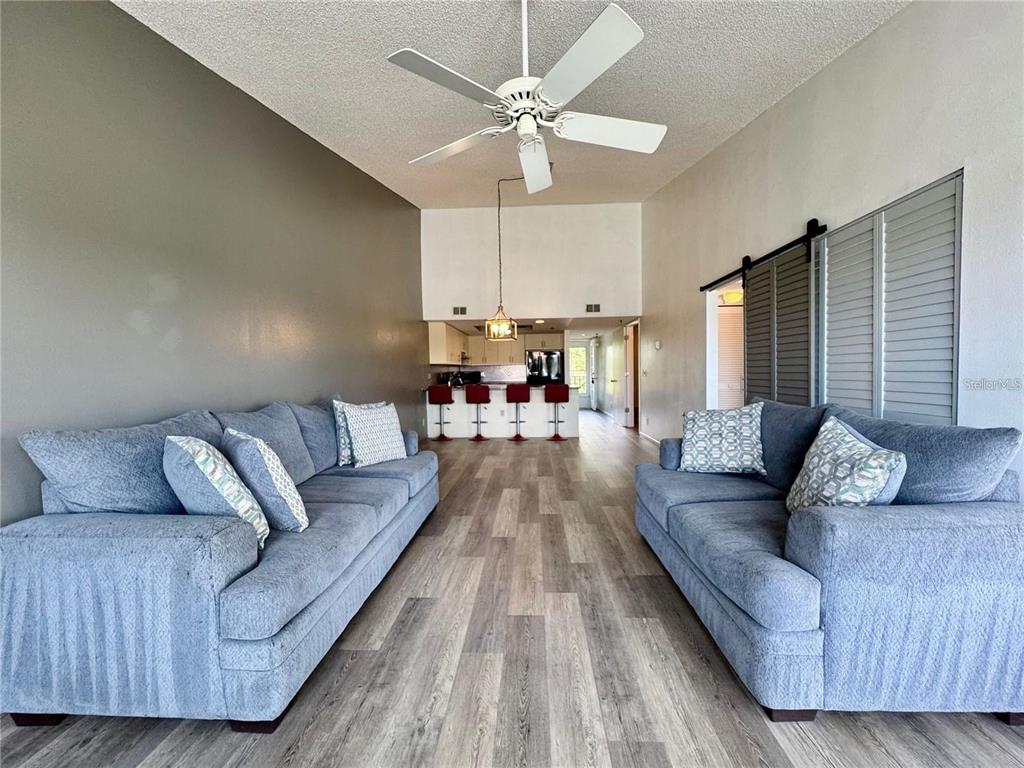 A living room with two blue sofas, wood-look flooring, and a kitchen in the background — 4510 EL CONQUISTADOR PARKWAY UNIT 204, BRADENTON, FL