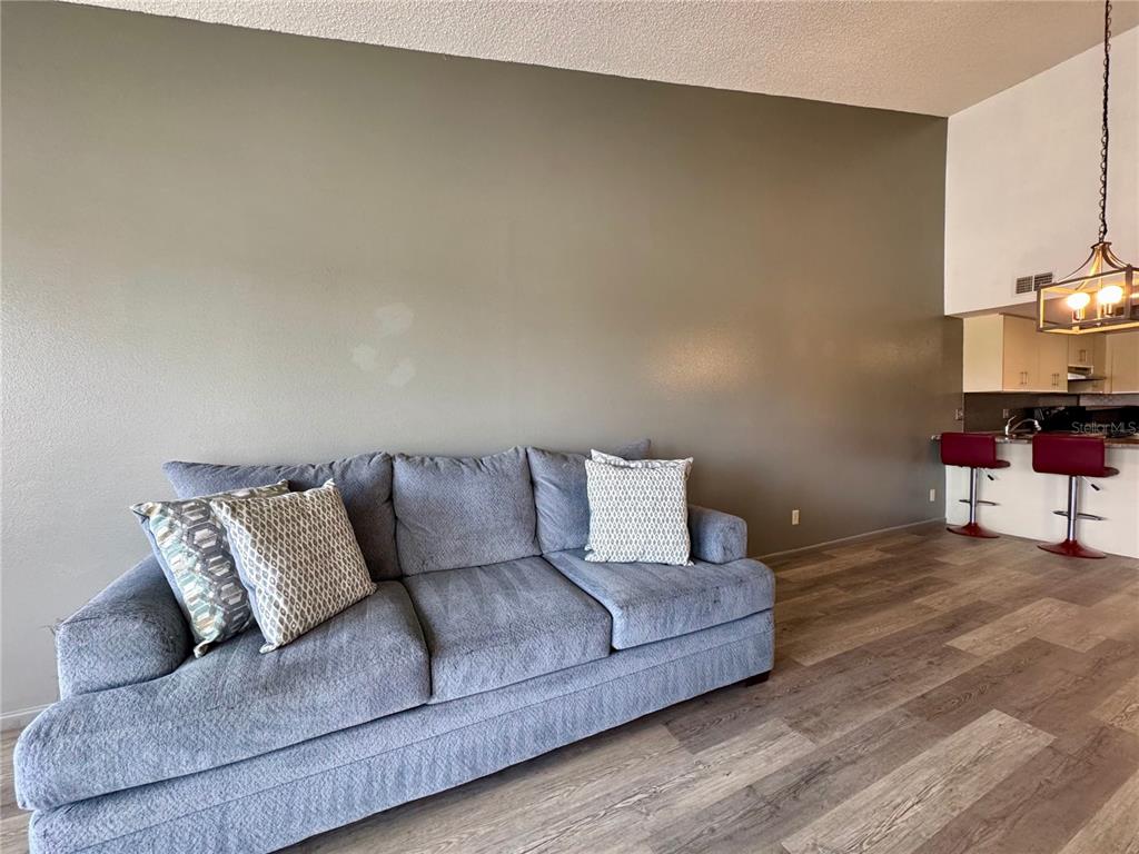 A living room features a gray sofa, wood-look flooring, and a kitchen breakfast bar — 4510 EL CONQUISTADOR PARKWAY UNIT 204, BRADENTON, FL