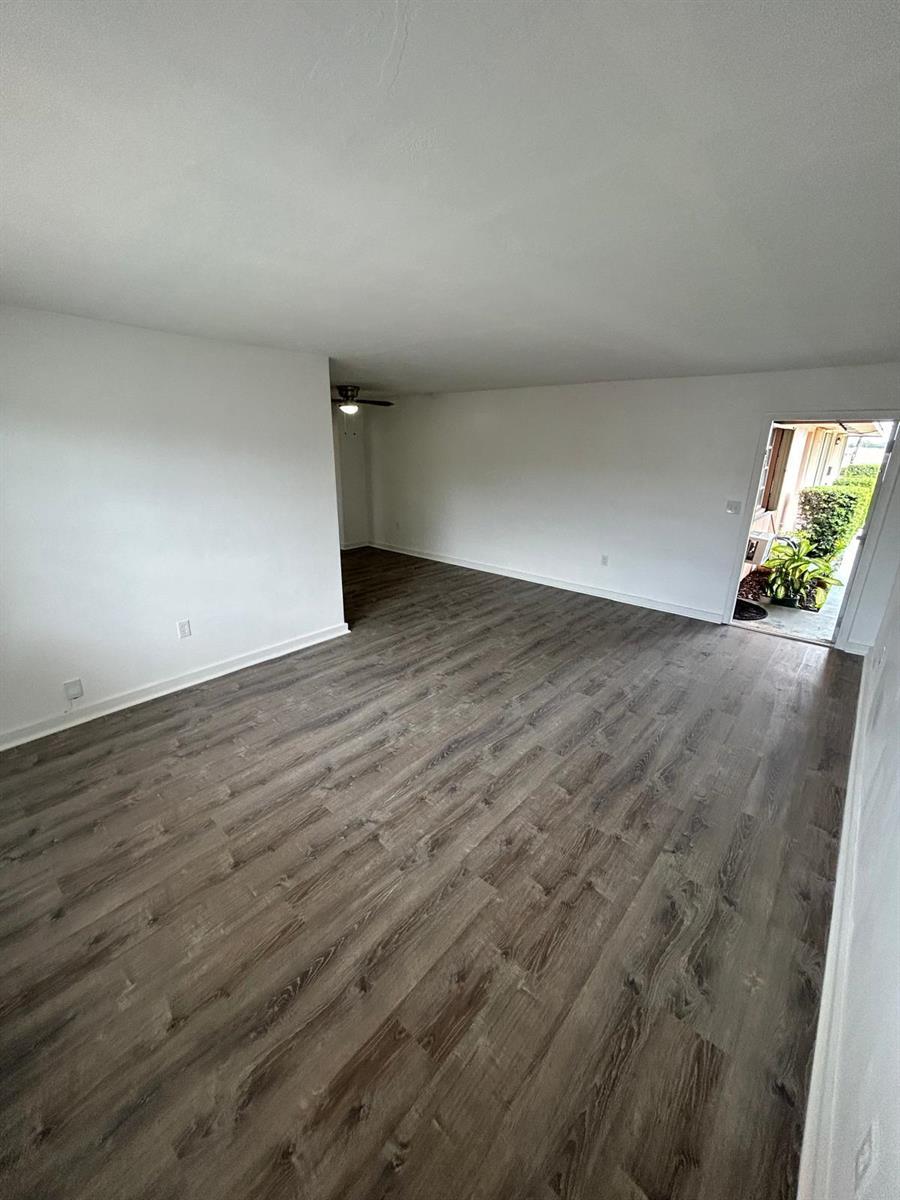 An empty living room features white walls, dark wood-look flooring, and an open exterior door — 7624 Pembroke Road # D, Miramar FL 33023, MIRAMAR, FL