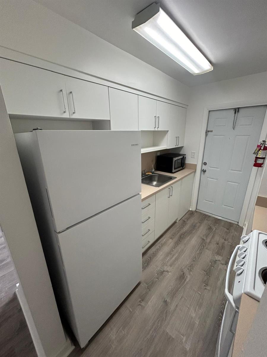 A galley kitchen features white cabinets, a refrigerator, a sink, and light wood-look flooring — 7624 Pembroke Road # D, Miramar FL 33023, MIRAMAR, FL