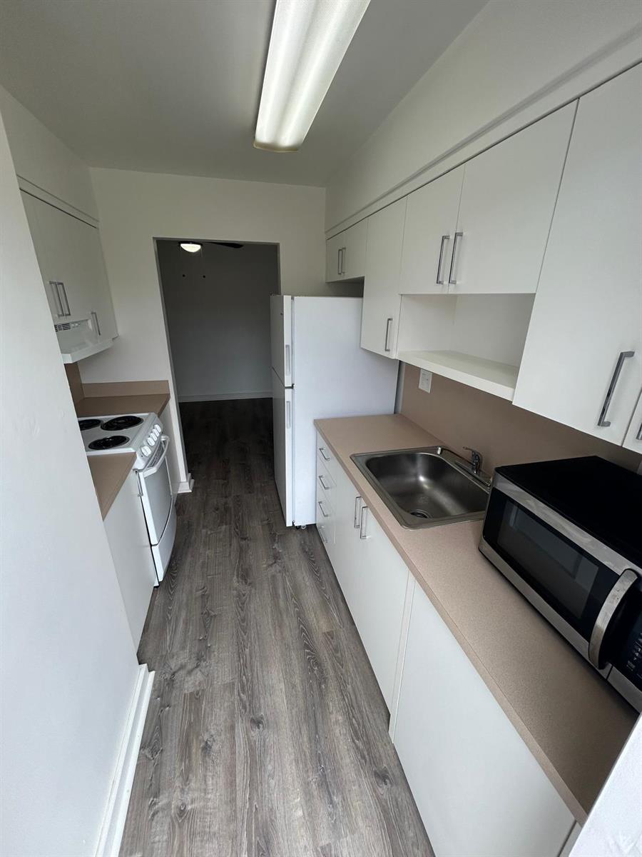 A galley-style kitchen features white cabinets, tan countertops, stainless steel appliances, and wood-look flooring — 7624 Pembroke Road # D, Miramar FL 33023, MIRAMAR, FL