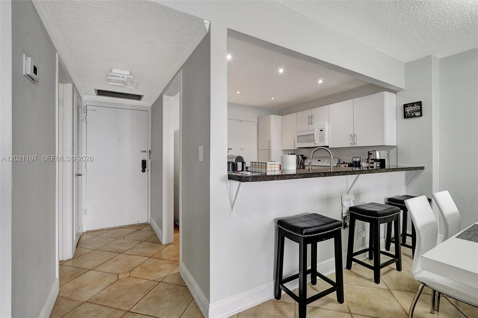 A kitchen with white cabinets and a breakfast bar overlooks a tiled entryway — 3725 S Ocean Dr # 812, Hollywood FL 33019, HOLLYWOOD, FL