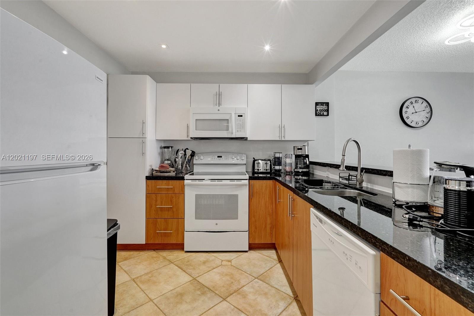 A kitchen features white upper cabinets, wood lower cabinets, black countertops, and white appliances — 3725 S Ocean Dr # 812, Hollywood FL 33019, HOLLYWOOD, FL
