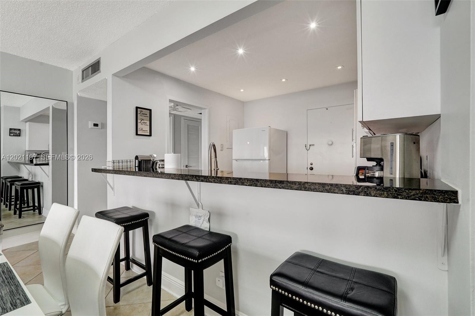 A kitchen features a dark granite breakfast bar with black stools and white cabinetry — 3725 S Ocean Dr # 812, Hollywood FL 33019, HOLLYWOOD, FL