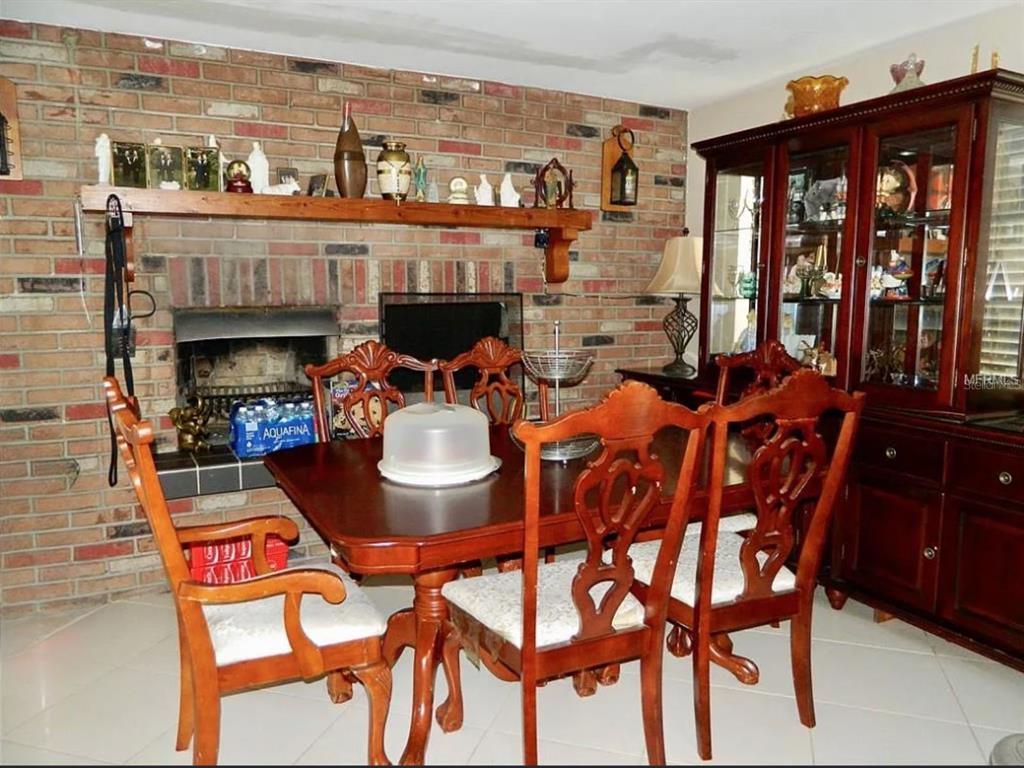 A dining room features a brick fireplace, a wooden table with chairs, and a china cabinet — 3442 WILTSHIRE DRIVE, HOLIDAY, FL