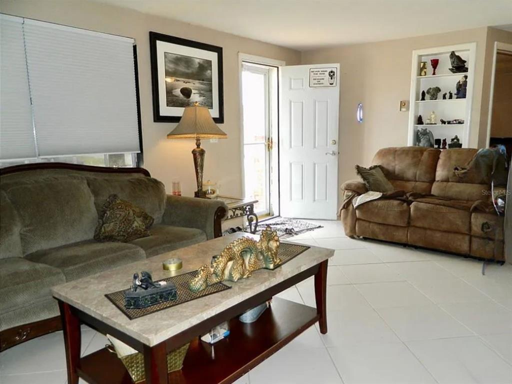 A living room features two sofas, a coffee table with dragon figurines, and white tile flooring — 3442 WILTSHIRE DRIVE, HOLIDAY, FL